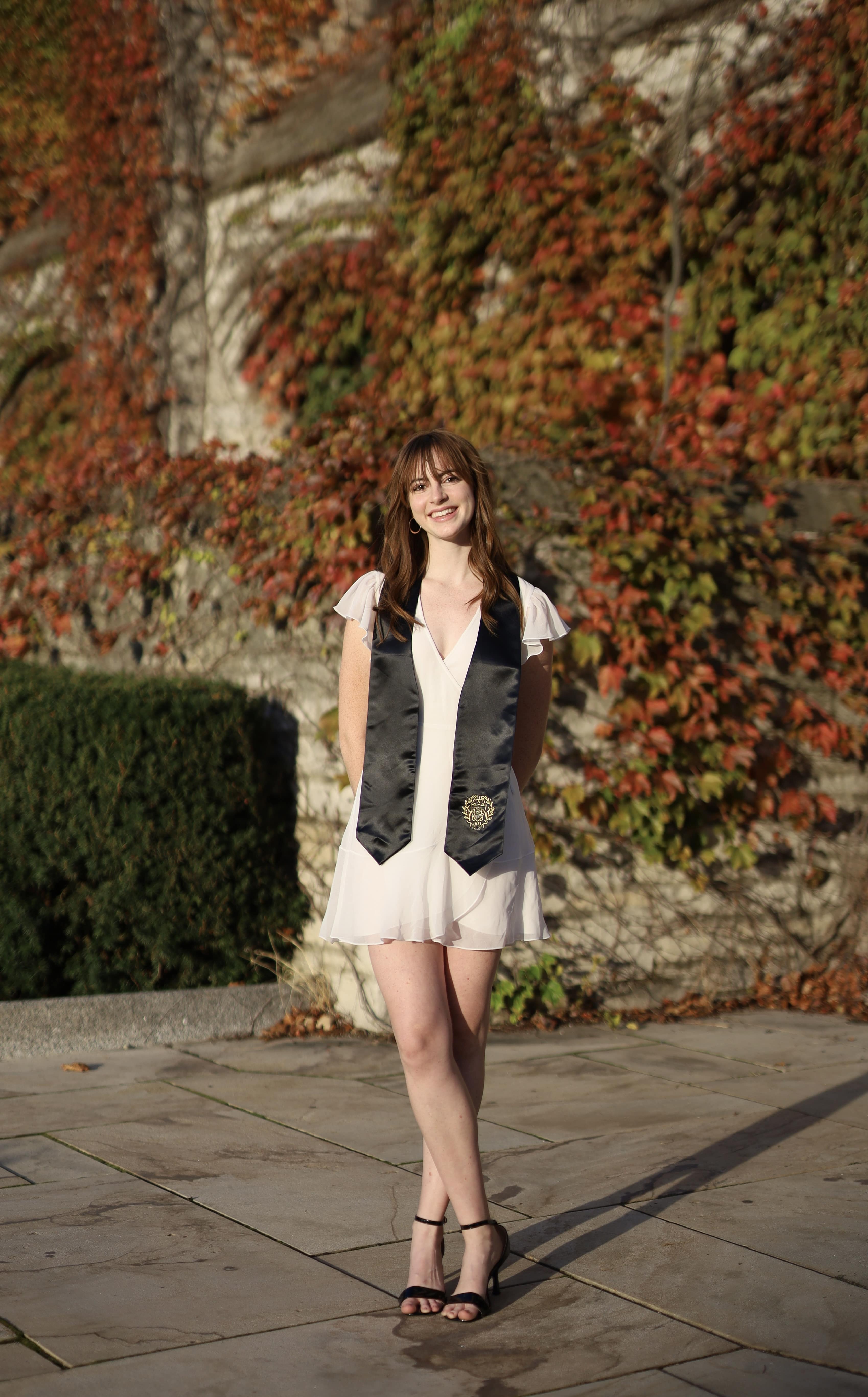 Elena standing in a white dress with a grad sash